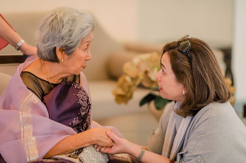 An adult daughter holding her mother's hands while they talk at home