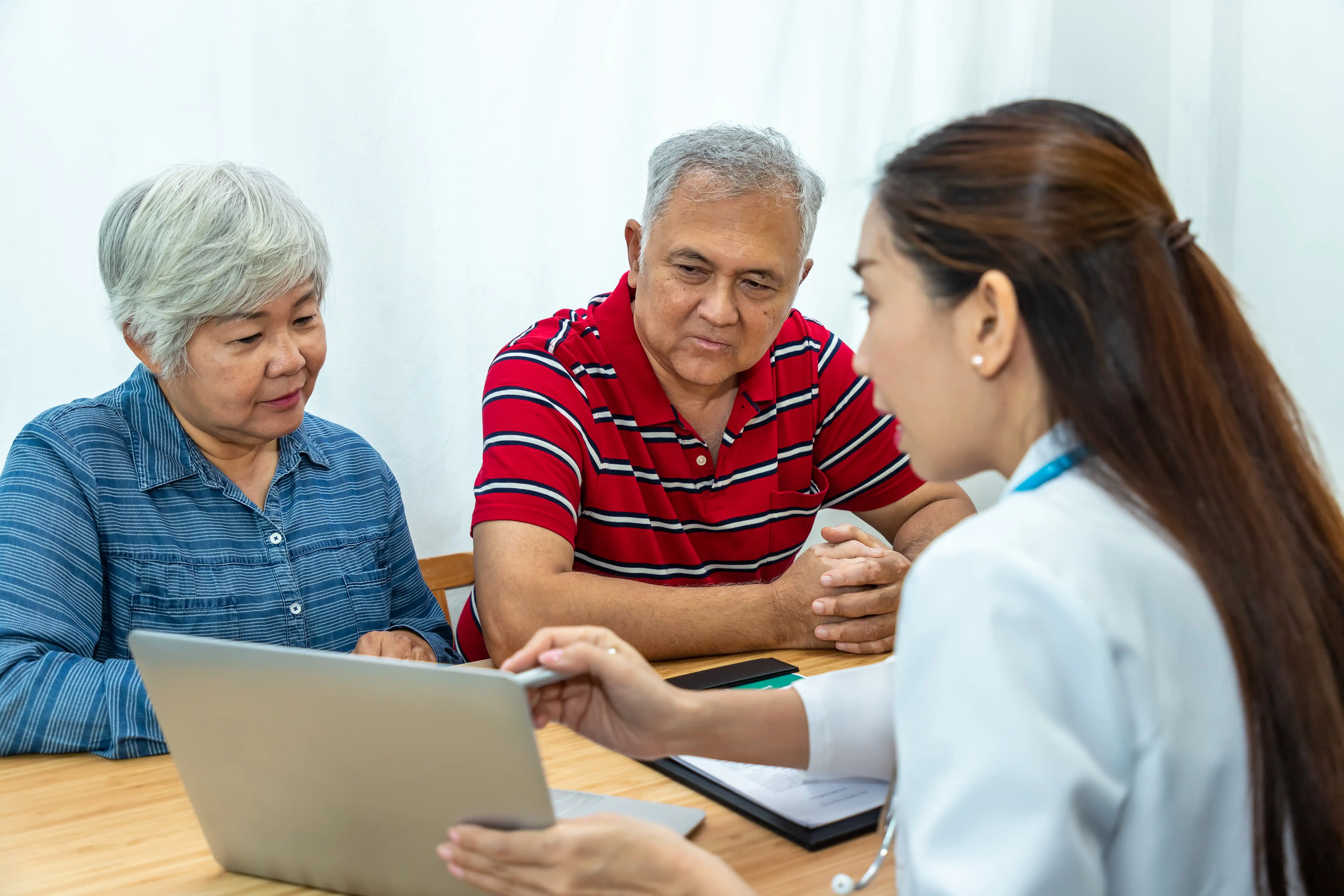 Asian doctor discussing health concerns with an elderly couple in a medical office setting.